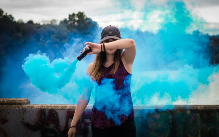 What we do A stylish woman surrounded by bright blue smoke outdoors, creating a dynamic fashion statement.